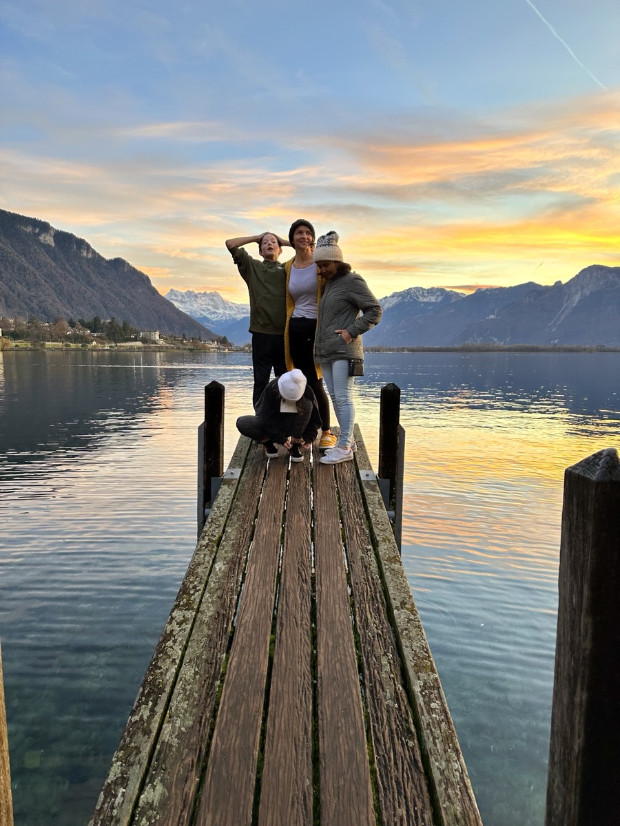 Julia, her kids, and her mom on a dock in Switzerland at sunset.